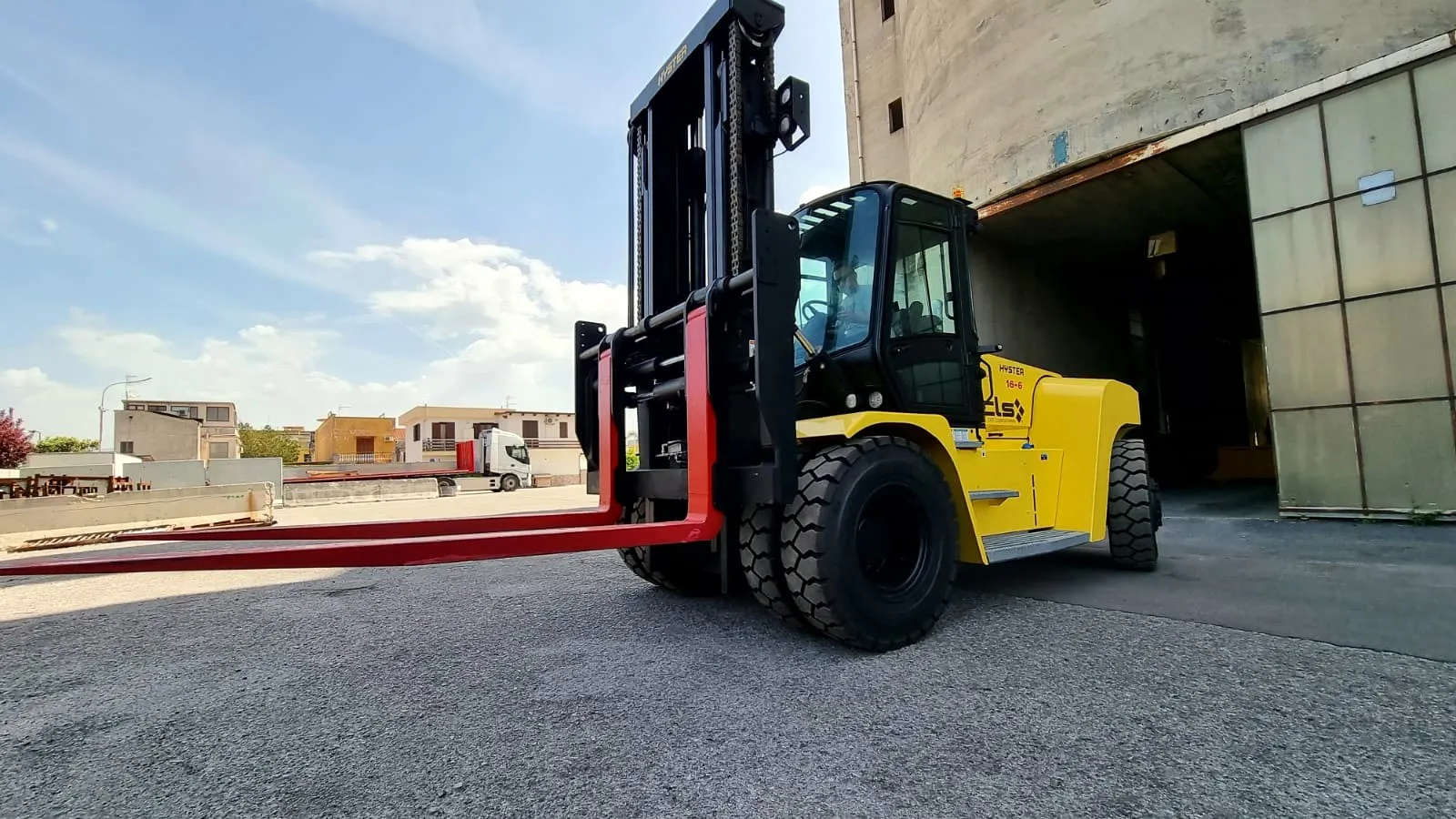 Carrello elevatore giallo da 16 tonnellate con forche rosse, davanti a un magazzino