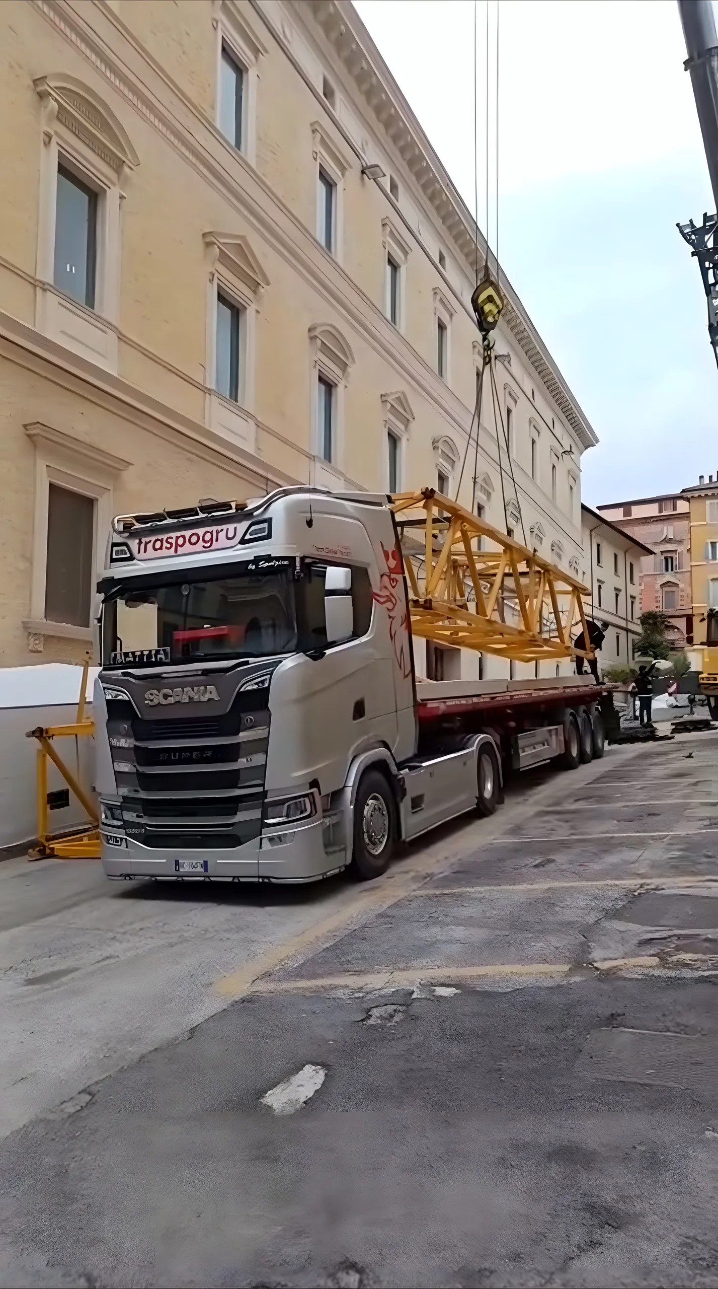 Scania Traspogru in una via del centro storico mentre una gru scarica un tronco di gru a torre
