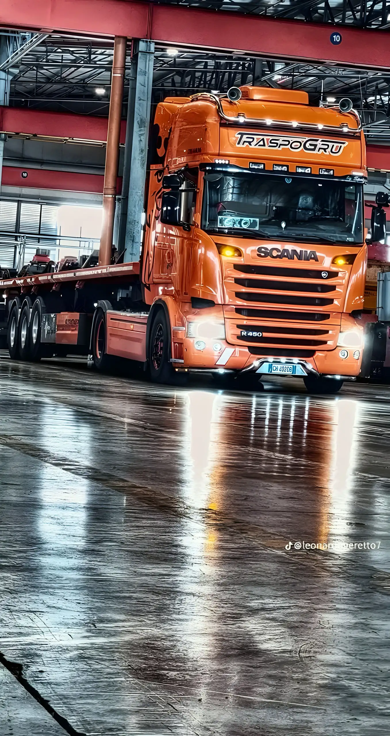 Scania R450 arancione Traspogru con fari accesi su un pavimento bagnato